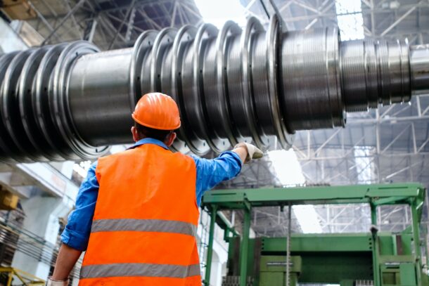 worker in hardhat and reflective vest inspecting large metal machinery indoors